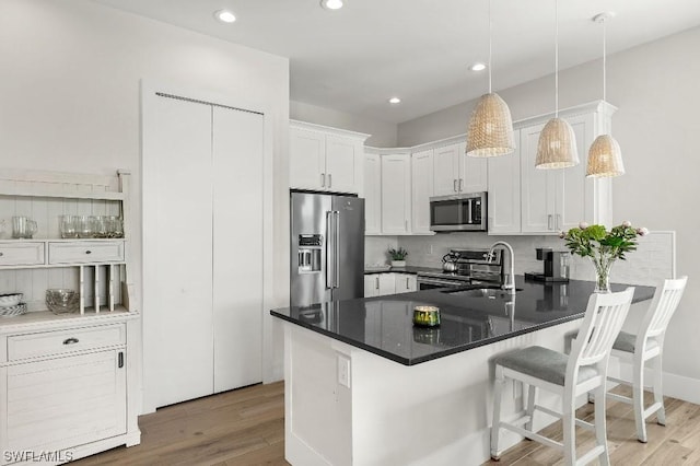 kitchen featuring light wood finished floors, a peninsula, stainless steel appliances, white cabinets, and backsplash