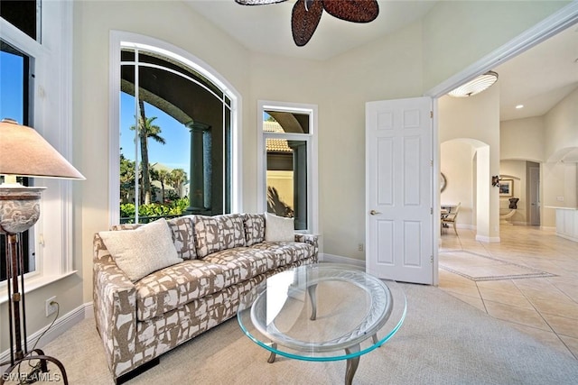 living area featuring a ceiling fan, light tile patterned flooring, arched walkways, and baseboards