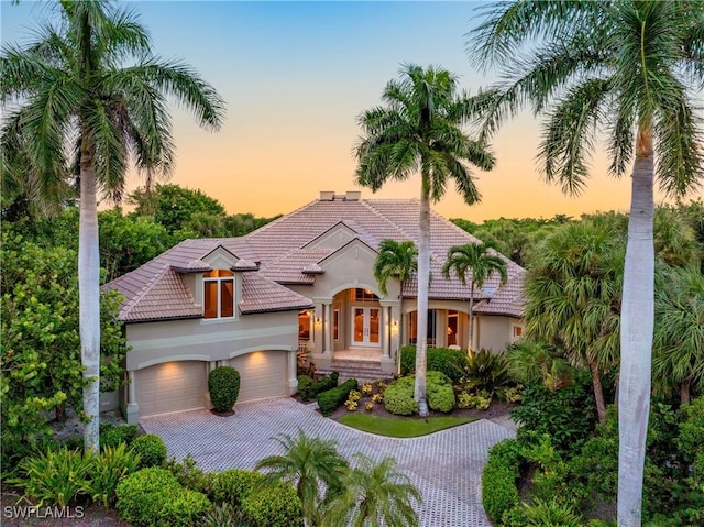 mediterranean / spanish home featuring decorative driveway, an attached garage, a tiled roof, and stucco siding