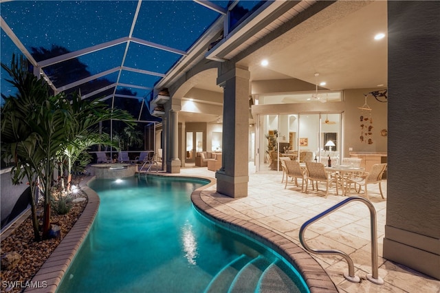 pool at night featuring ceiling fan, glass enclosure, and a patio area