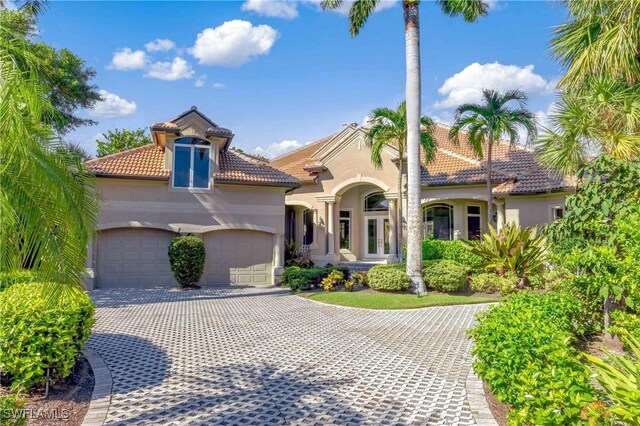 mediterranean / spanish-style home featuring decorative driveway, a tile roof, stucco siding, and a garage
