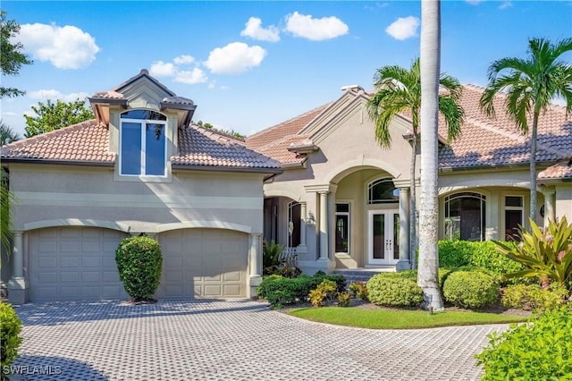 mediterranean / spanish-style home with french doors, decorative driveway, a tiled roof, and stucco siding