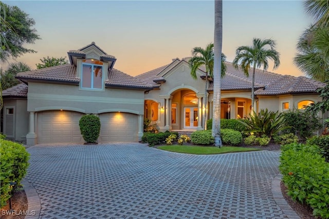 mediterranean / spanish house with decorative driveway, stucco siding, a garage, and french doors