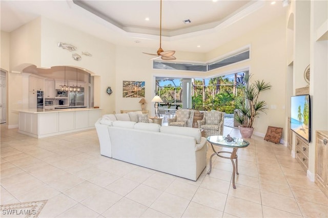 living room featuring a tray ceiling, light tile patterned floors, a high ceiling, arched walkways, and a ceiling fan