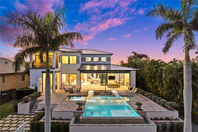 rear view of property with metal roof, a balcony, a patio area, an in ground hot tub, and a standing seam roof