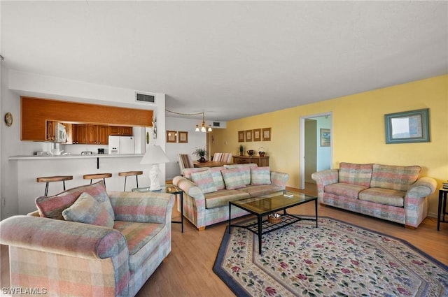 living area featuring visible vents, light wood-style flooring, and an inviting chandelier