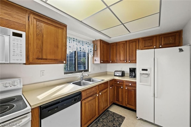 kitchen featuring light countertops, white appliances, brown cabinetry, and a sink