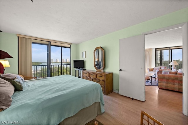 bedroom with access to outside, a wall of windows, and light wood-type flooring