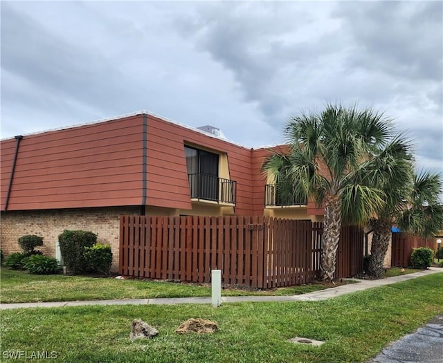 view of side of property featuring brick siding, a yard, a balcony, and fence