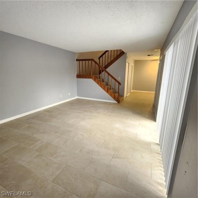 unfurnished living room with baseboards, a textured ceiling, and stairs