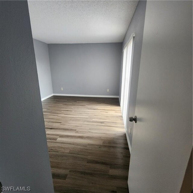 empty room featuring a textured ceiling, baseboards, and wood finished floors