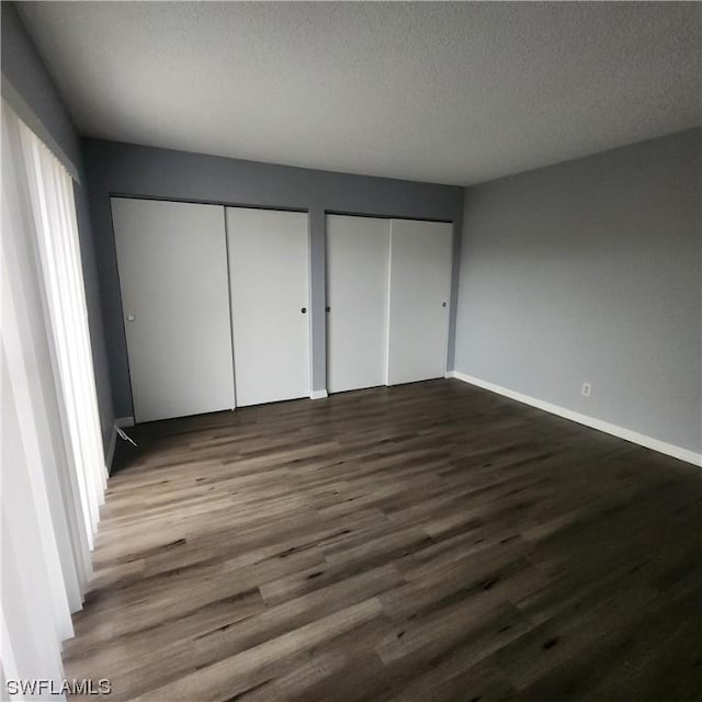 unfurnished bedroom featuring baseboards, multiple closets, a textured ceiling, and dark wood finished floors