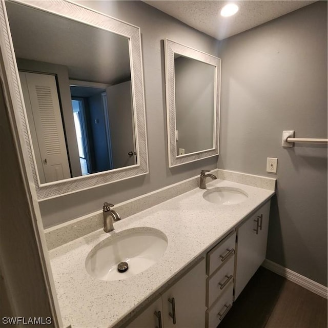 bathroom featuring double vanity, wood finished floors, baseboards, and a sink