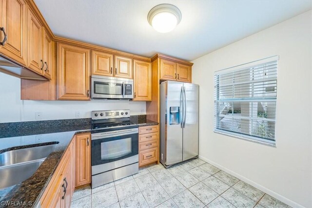 kitchen with appliances with stainless steel finishes, light tile patterned floors, and dark stone counters