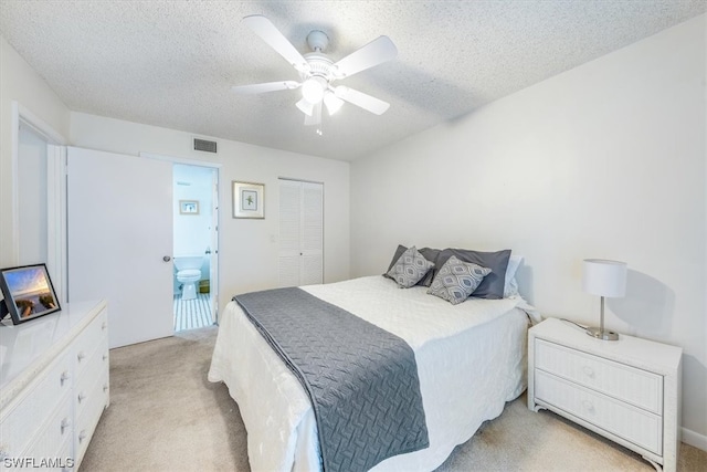 bedroom featuring a textured ceiling, ceiling fan, light colored carpet, ensuite bathroom, and a closet