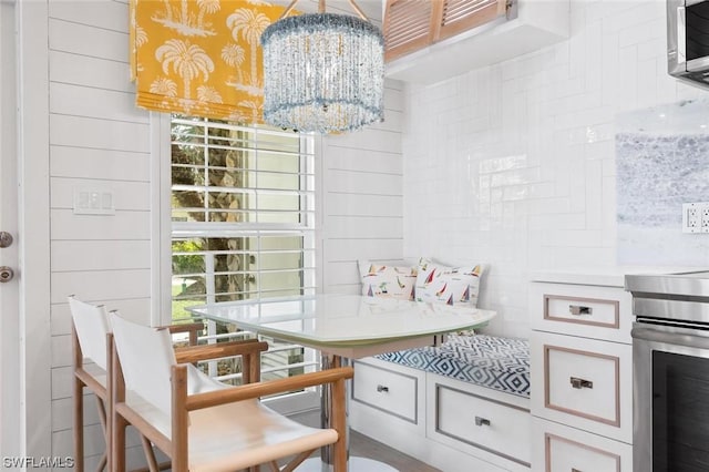 interior space with wooden walls, white cabinetry, a chandelier, hanging light fixtures, and breakfast area