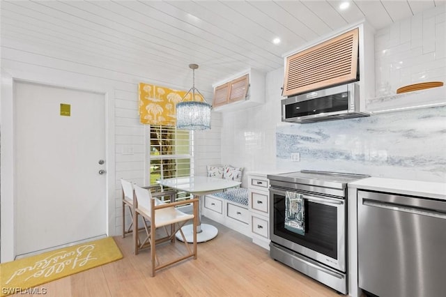 kitchen featuring light wood-style flooring, appliances with stainless steel finishes, breakfast area, light countertops, and backsplash