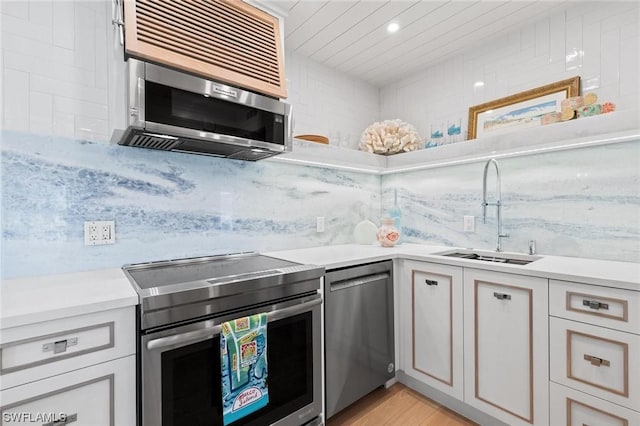 kitchen with light countertops, decorative backsplash, appliances with stainless steel finishes, a sink, and light wood-type flooring