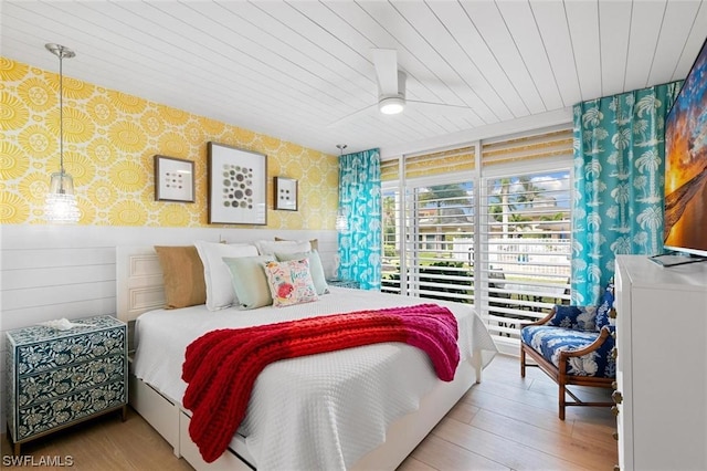 bedroom with wallpapered walls, wood ceiling, wood finished floors, and a wainscoted wall