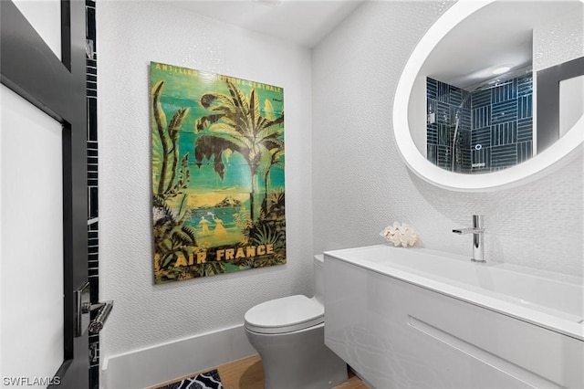 bathroom with a textured wall, wood finished floors, vanity, and toilet