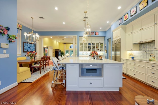 kitchen with dark wood finished floors, glass insert cabinets, appliances with stainless steel finishes, backsplash, and a notable chandelier