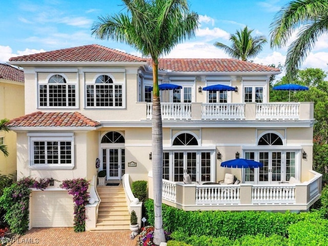 rear view of property with french doors, a balcony, and stucco siding