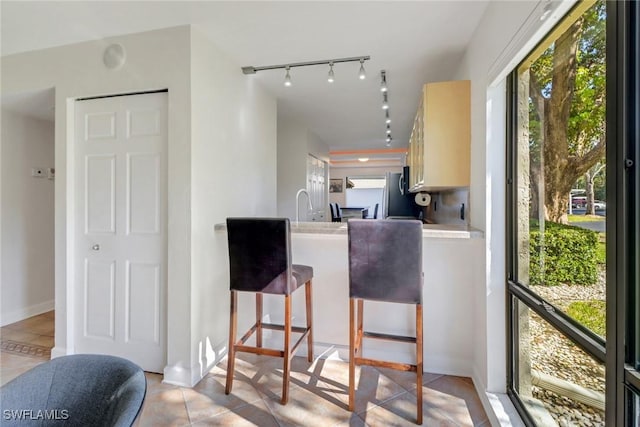 kitchen featuring a breakfast bar area, stainless steel fridge, light brown cabinets, and light tile patterned floors