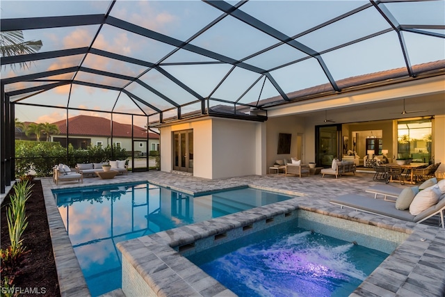 pool at dusk with an in ground hot tub, an outdoor hangout area, glass enclosure, and a patio