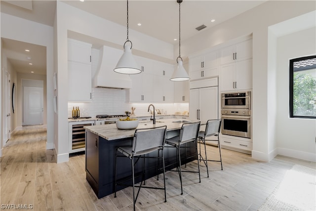 kitchen featuring wine cooler, custom range hood, white cabinetry, and an island with sink