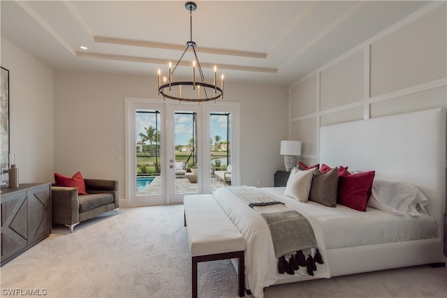 bedroom featuring an inviting chandelier, light colored carpet, a tray ceiling, and access to exterior