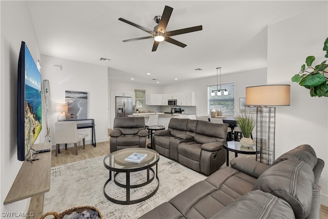 living room featuring ceiling fan with notable chandelier and light hardwood / wood-style flooring