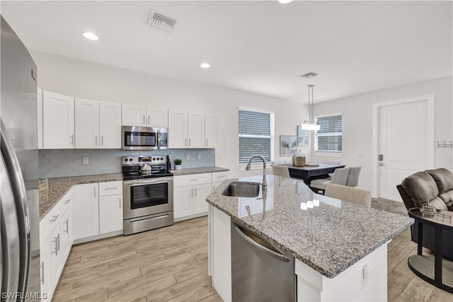 kitchen with light stone countertops, decorative light fixtures, backsplash, sink, and stainless steel appliances