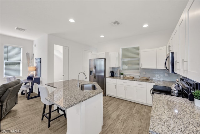 kitchen with an island with sink, sink, appliances with stainless steel finishes, backsplash, and a breakfast bar area