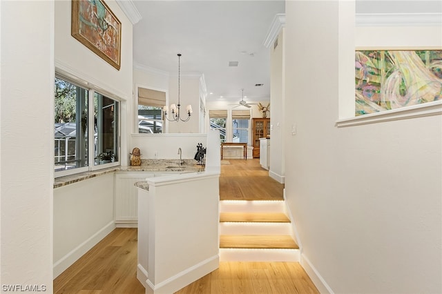 kitchen with pendant lighting, white cabinets, light wood-type flooring, ornamental molding, and a chandelier