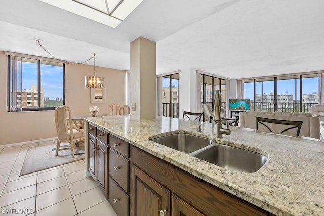 kitchen featuring hanging light fixtures, light stone countertops, a skylight, light tile patterned flooring, and sink