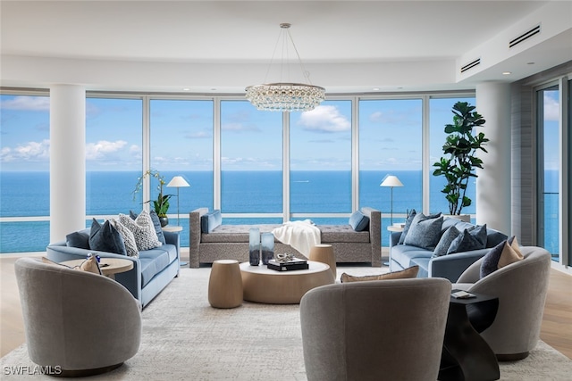 living room featuring an inviting chandelier, a water view, floor to ceiling windows, and wood-type flooring