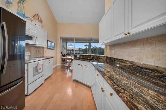 kitchen with white appliances, white cabinets, light hardwood / wood-style flooring, decorative backsplash, and dark stone countertops