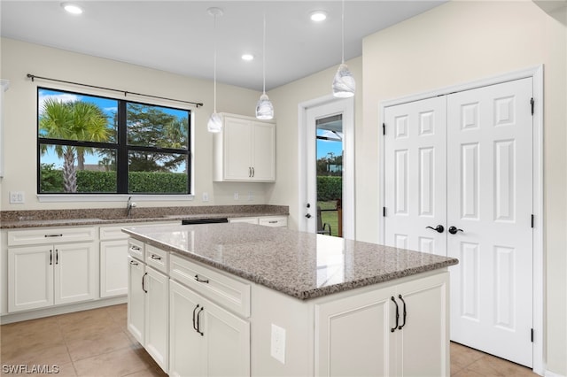 kitchen featuring white cabinets, sink, hanging light fixtures, light stone countertops, and a kitchen island