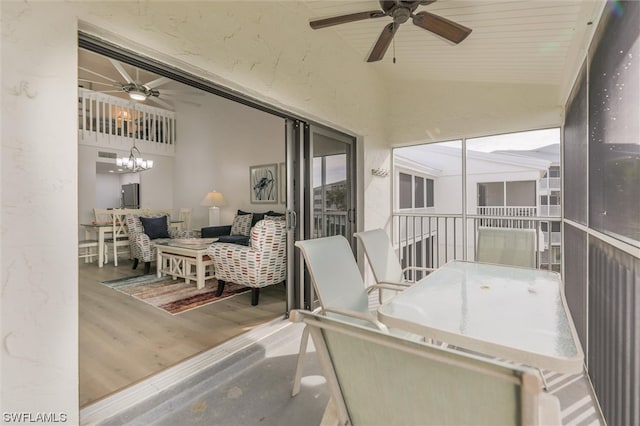 sunroom featuring ceiling fan with notable chandelier and lofted ceiling