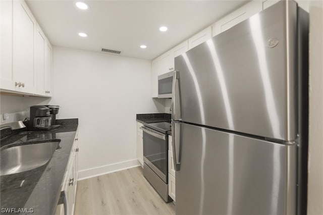 kitchen featuring dark stone countertops, appliances with stainless steel finishes, light hardwood / wood-style floors, and white cabinetry