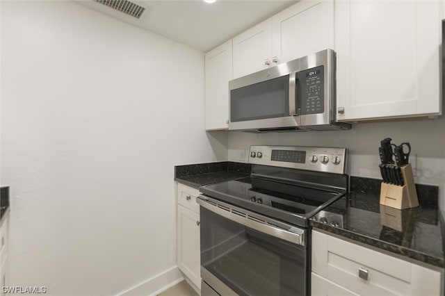 kitchen featuring dark stone countertops, appliances with stainless steel finishes, and white cabinetry