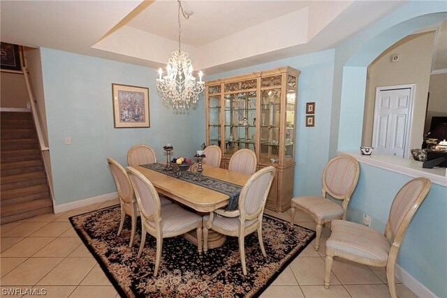 tiled dining area with a raised ceiling and a notable chandelier