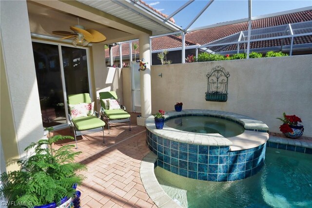 view of patio with ceiling fan, a swimming pool with hot tub, and glass enclosure