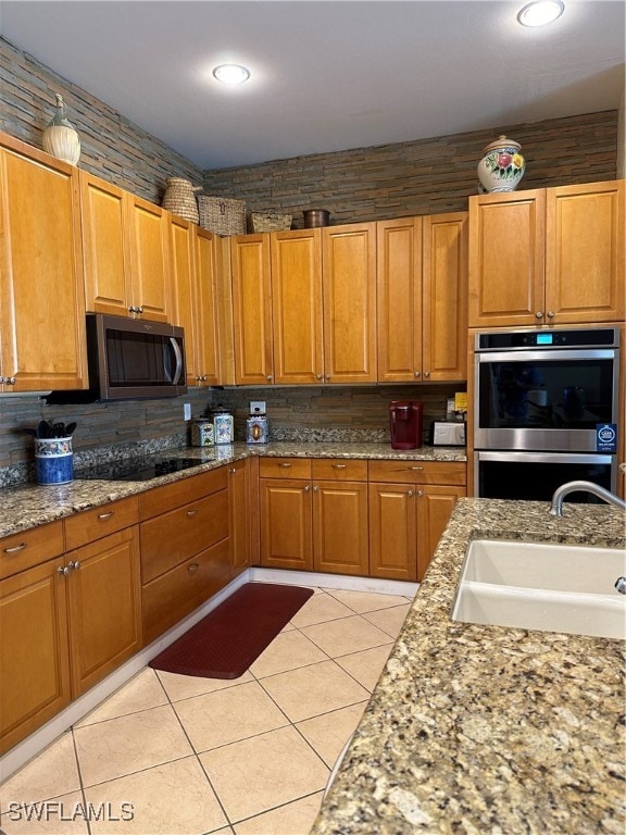 kitchen with tasteful backsplash, sink, light stone countertops, appliances with stainless steel finishes, and light tile patterned floors