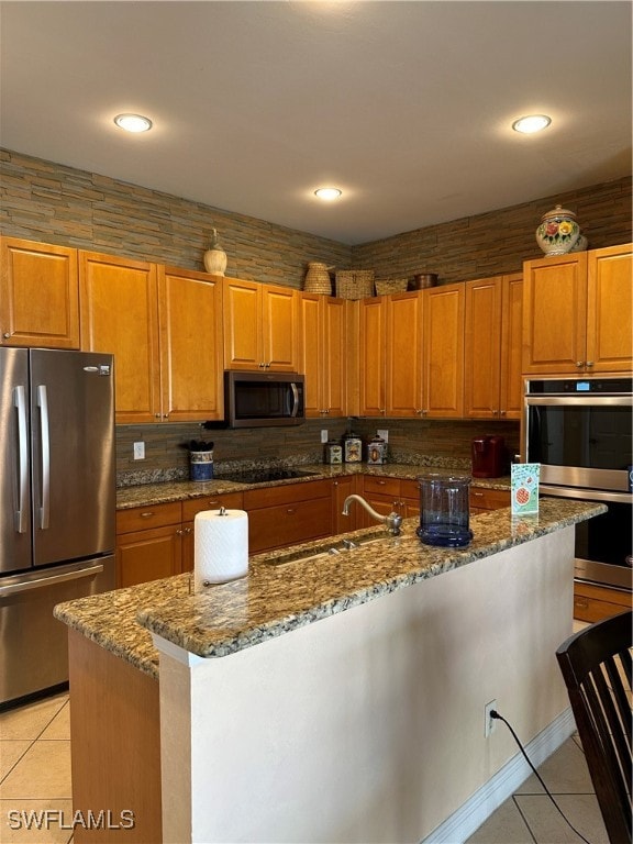 kitchen featuring appliances with stainless steel finishes, dark stone countertops, light tile patterned floors, and a kitchen island with sink