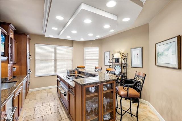 kitchen with an island with sink, black cooktop, dark stone countertops, and a kitchen bar