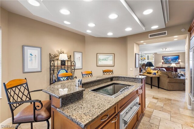 kitchen featuring an island with sink, black electric stovetop, light stone counters, and a kitchen breakfast bar