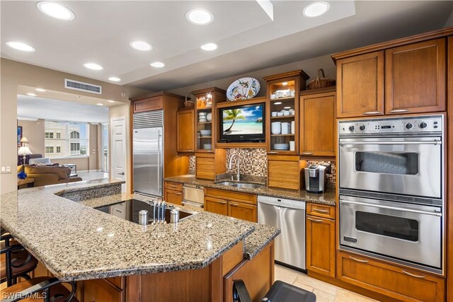 kitchen with a spacious island, sink, light stone counters, appliances with stainless steel finishes, and a kitchen breakfast bar