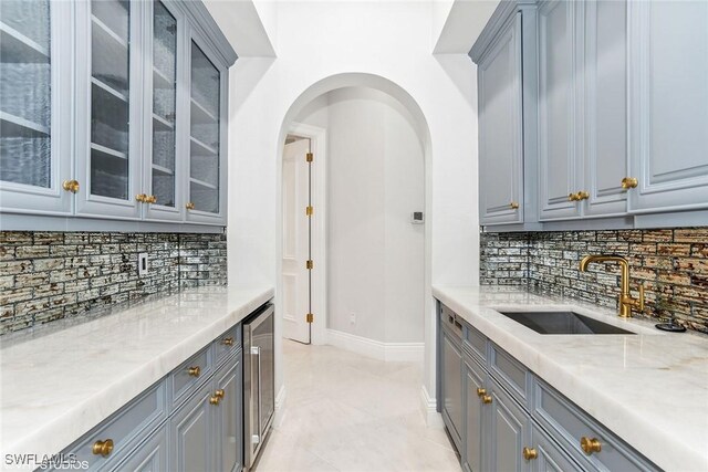 kitchen with gray cabinetry, backsplash, sink, light stone counters, and beverage cooler