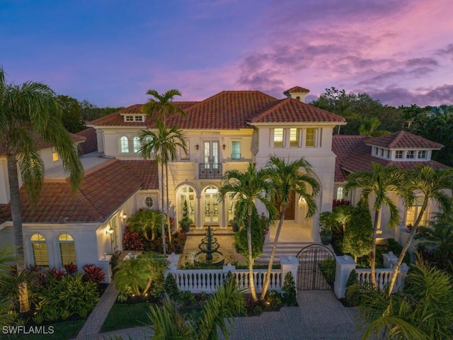 mediterranean / spanish house featuring a gate, a fenced front yard, french doors, a balcony, and a tiled roof